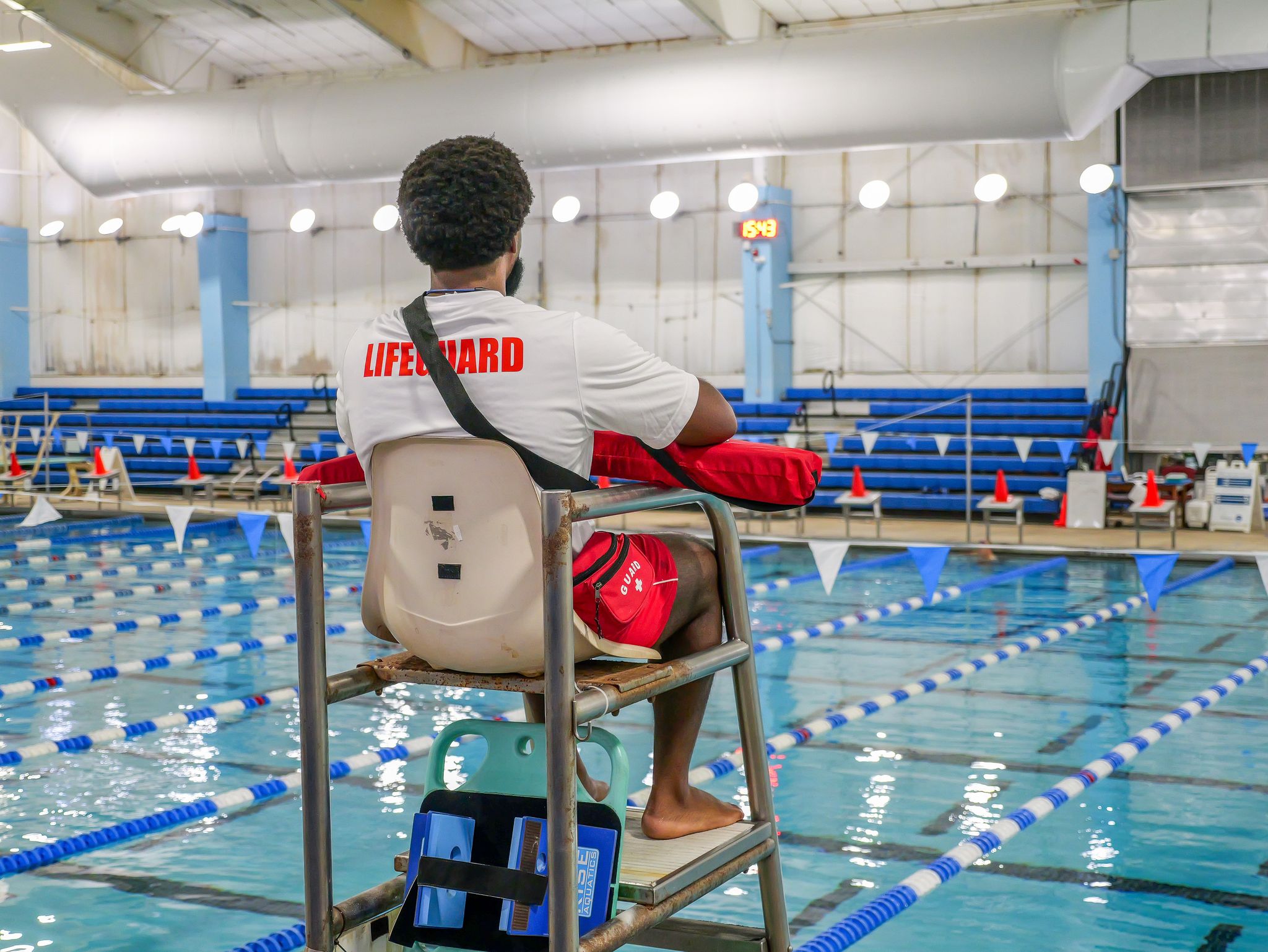 Male lifeguard sitting in chair stand overlooking an indoor pool